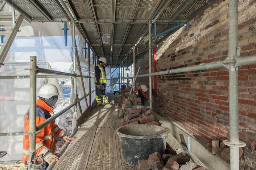 Bouwplaats waar twee bouwvakkers op een steiger werken aan een geven